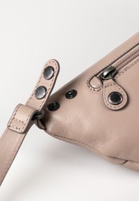 Beige Lederhandtasche mit einem Reißverschluss, Metallbeschlägen und verstellbarem Trageriemen. Verfügt über eine abgerundete Form und sichtbare Nähte.