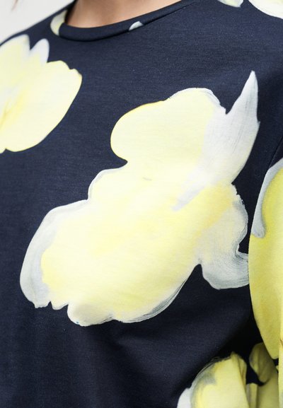 Μπλε πουκάμισο με μεγάλο, αφηρημένο κίτρινο λουλουδένιο μοτίβο, κοντά μανίκια και στρογγυλή λαιμόκοψη, κατασκευασμένο από μαλακό βαμβακερό ύφασμα.