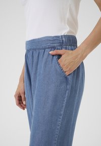 Pantalones de mezclilla azul claro con cinturilla elástica, que cuentan con un bolsillo lateral y un ajuste relajado, destacando una textura suave y lisa.