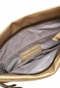 Gold synthetic leather bag interior featuring a smooth gray lining, zippered pocket, and distinct logo tag.