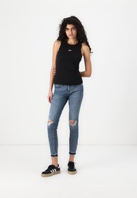 Crna majica bez rukava s logotipom "GAP", uparena s svijetloplavim poderanim skinny trapericama i crnim tenisicama s bijelim prugama.