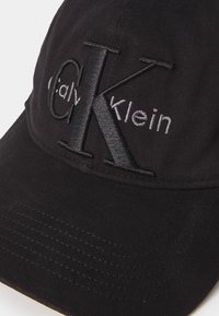 Zwarte baseballpet van katoen, met een reliëf "CK" logo in zwart en "Calvin Klein" in grijs, afgewerkt met een gestructureerde stof.