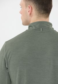 Groene langarmige shirt met een hoge kraag en een subtiele textuur. Opvallende details zijn een kleine gestreepte accent bij de halslijn.