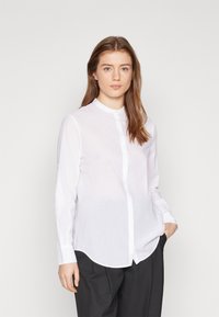 Camicia bianca a button-up con colletto arrotondato e maniche lunghe, realizzata in tessuto leggero; presenta un orlo dritto e una sottile trama.