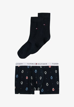 Pakke med sorte sokker og Tommy Hilfiger boxershorts, der har et mønster med farvede logoer, hvid talje og blød stoftekstur.