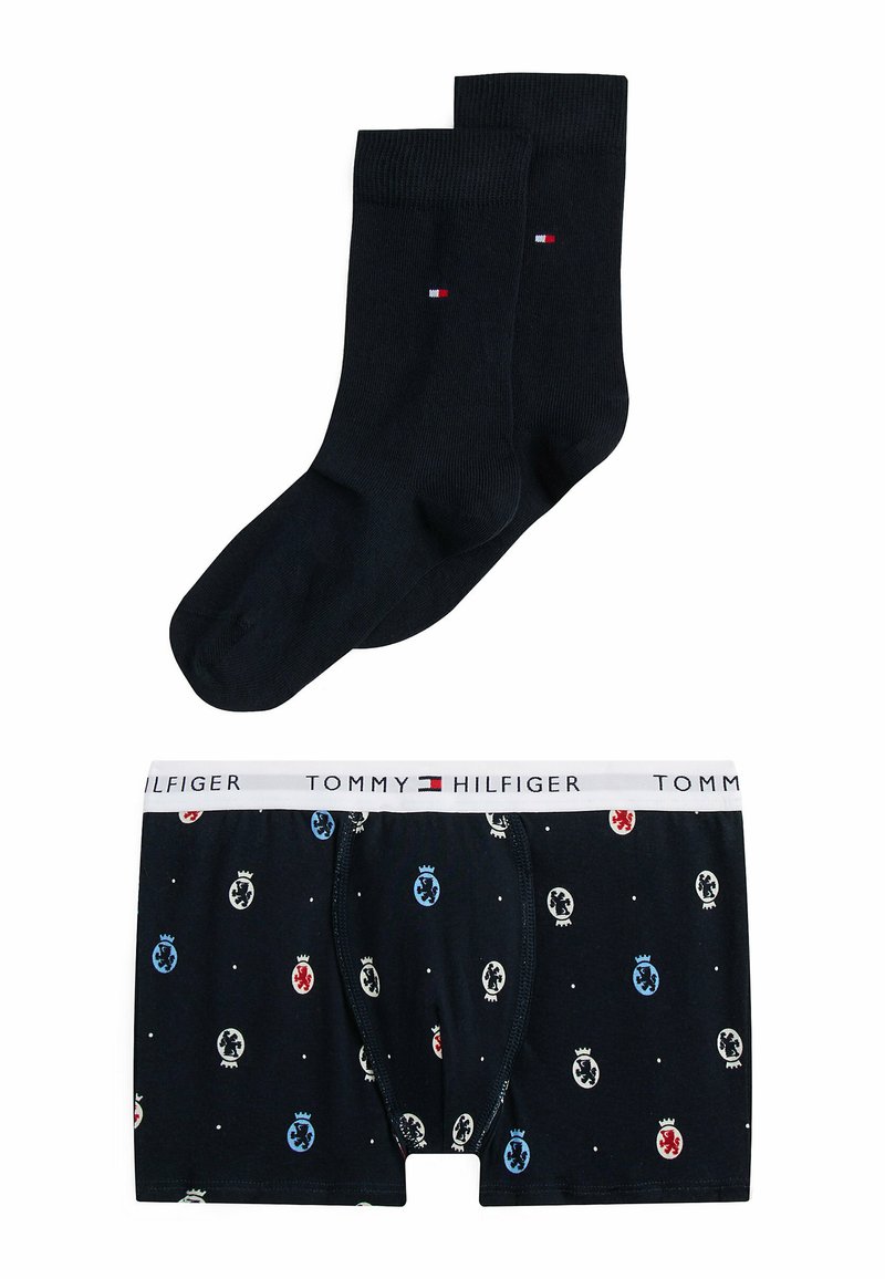 Pakke med sorte sokker og Tommy Hilfiger boxershorts, der har et mønster med farvede logoer, hvid talje og blød stoftekstur.