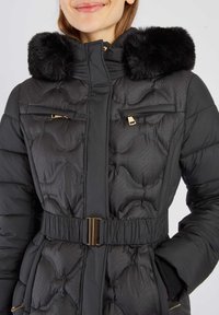 Czarna kurtka puchowa z kapturem wykończonym futrem, pikowany materiał, złote elementy i pasek w talii. Kieszenie na zamek na klatce piersiowej.