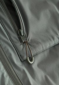 O țesătură gri cu o textură netedă are un detaliu cu fermoar și un șnur maro. Fermoarul este integrat în material.