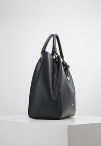 Svart läderhandväska med en pebblig yta, avslappnad form, dubbla topphandtag och detaljer i guldfärg. Har en dekorativ charm.