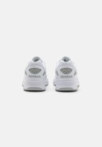 Fehér Reebok sportcipő szürke kiegészítőkkel. Lélegző mesh felsőrésszel, párnázott nyakkal és texturált talppal rendelkezik a stabilitás érdekében.