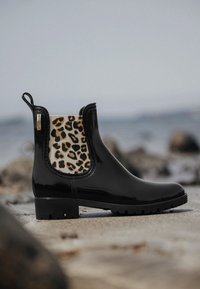 Botín de charol negro con panel elástico de leopardo, punta redondeada, lengüeta y suela texturizada para mayor tracción.