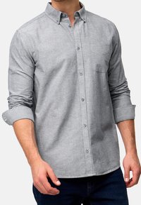 Szara koszula z guzikami, wykonana z miękkiego materiału; posiada kołnierzyk, jedną kieszeń na piersi i podwinięte rękawy, prezentując gładką teksturę.