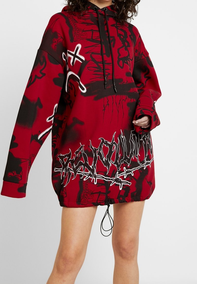 Yli-iso punainen huppari, jossa on mustat graffity-tyyliset grafiikat ja piikkilanka-yksityiskohdat. Varustettu säädettävällä hupulla ja resorikäänteillä.