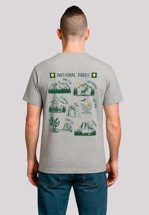 Gray t-shirt featuring green illustrations of various national parks, including mountains, trees, and wildlife, with text at the top.