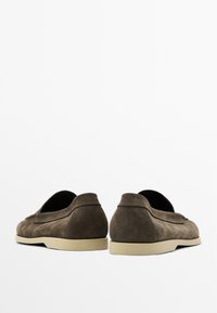 Chaussures slip-on en suede marron avec un bout arrondi, un design minimaliste et une semelle en caoutchouc de couleur claire en contraste. Texture douce et détail de couture simple.