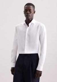 Witte overhemd met lange mouwen en een subtiele textuur, met een button-down kraag en manchetten. Gekozen in combinatie met marineblauwe broek, wat een formele stijl accentueert.