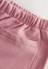 Tissu rose à finition texturée, avec une taille élastique et une poche latérale. Les coutures sont visibles le long des bords.