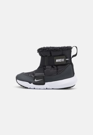 Schwarze und graue Nike Winterstiefel mit weißer Sohle, gepolstertem Schaft, verstellbarem Riemen, Schaffellfutter und Zugschlaufe an der Ferse.