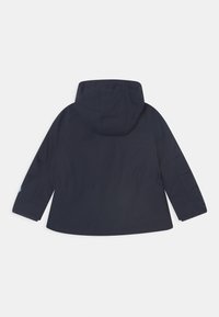 Marinblå huvrjacka med lös passform, prydd med långa ärmar och en rak nederkant. Tillverkad av glatt, vattenavvisande material.