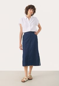 Camisa de lino blanca de manga corta con botones amarillos, combinada con una falda midi a rayas azul marino y sandalias beige.