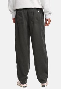 Graue Baumwollhosen mit lässiger Passform, ausgestattet mit zwei Gesäßtaschen und einem elastischen Bund. Das Material hat eine weiche, strukturierte Oberfläche.