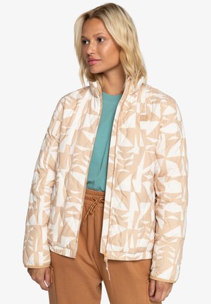 Quilted jacket in beige with white geometric patterns, featuring a zip front, a stand collar, and elastic cuffs. Worn over a teal shirt.