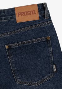 Granatowe dżinsy wykonane z denimu z skórzaną naszkółką marki "PROSTO." oraz jedną tylną kieszenią z widocznymi detalami szycia.