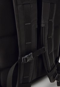 Svart ryggsäck med slitstarkt tyg, vadderade remmar, plastspännen och flera justerbara remmar för säker fastsättning.