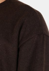 Maglione a collo rotondo di colore marrone scuro in maglia, con una finitura testurizzata e spalle strutturate. Tessuto morbido con un sottile motivo.