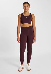 Bordeaux sportset bestaande uit een crop top met een ronde halslijn en een legging met hoge taille, beide gemaakt van rekbaar materiaal. Witte logo-accenten.