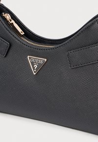 Czarna torebka Guess z fakturowanego materiału, z złotymi elementami i trójkątnym logo. Posiada zamknięcie na zamek oraz eleganckie, zaokrąglone kształty.