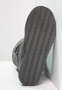 Boot gris avec une tige en suède texturé et une semelle en caoutchouc dotée d'un motif de semelle en zigzag. Accents latéraux et détails de couture visibles.