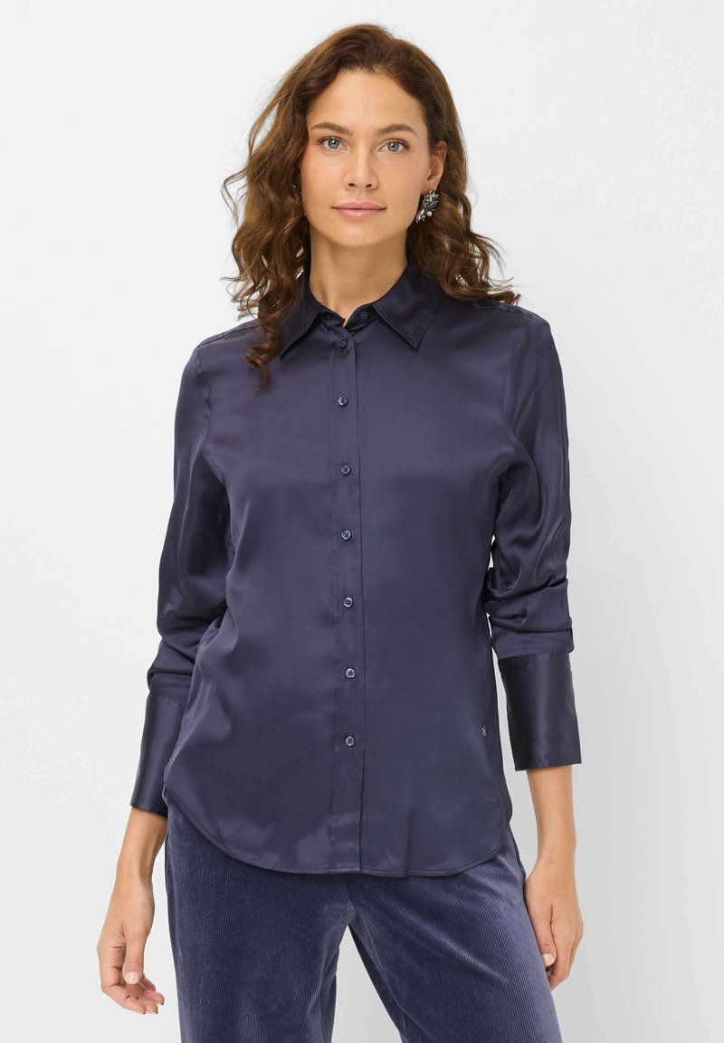 Navyblaue Satin-Schrift mit einem Umlegekragen, durchgehender Knopfleiste und langen Ärmeln, die eine glatte Textur und einen abgerundeten Saum aufweist.