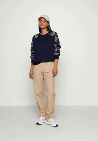 Navy floral sweatshirt with raglan sleeves, beige pants, and white sneakers with colorful accents. Light pink cap completes the outfit.
