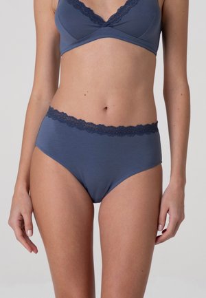 Torace femminile con reggiseno blu bordato in pizzo abbinato e mutandine a vita alta su uno sfondo chiaro semplice.