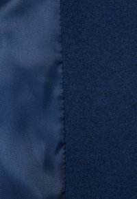 Marinblå tyg med en texturerad ylleblandning på ena sidan och slät satin på den andra, med en söm som löper vertikalt mellan dem.