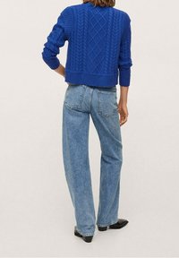 Pull bleu en maille torsadée avec poignets et ourlet côtelés, associé à un jean large bleu clair. Le pull présente un motif en losange texturé.