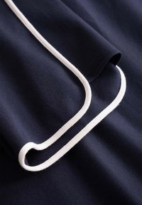 Tessuto blu scuro con piping bianco lungo il bordo, che mostra una superficie liscia e cuciture accurate in dettaglio ravvicinato.