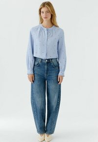 Hellblaue, kurze Bluse mit kleinen roten Herzmustern, langen Ärmeln und Knopfverschluss, kombiniert mit hoch taillierten, weit geschnittenen blauen Jeans.