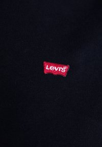 Čierna tkanina s malým červeným vyšitým logom Levi's s výrazným tvarom, umiestneným naľavo od stredu. Mäkká textúra, minimalistický dizajn.