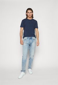 Μπλε βαμβακερό μπλουζάκι, ανοιχτό μπλε τζιν παντελόνι, λευκά αθλητικά παπούτσια. Απλό σχέδιο, στρογγυλή λαιμόκοψη, στενή εφαρμογή, ανοιχτόχρωμα τζιν με ξεθωριασμένες λεπτομέρειες.