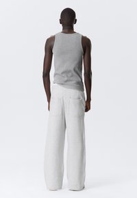 Grijze katoenen tanktop en lichtgrijze wijde sweatpants met twee achterzakken. Gladde stof, ontspannen pasvorm en eenvoudig ontwerp.