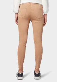 Pantalones cargo ajustados en un color marrón claro, con bolsillos laterales, bolsillos traseros y una textura suave. Combinados con zapatillas negras.