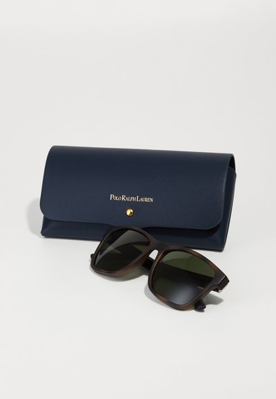 Polo Ralph Lauren saulesbrilles tumši brūnā plastikā ar zaļiem stikliem, komplektā ar tumši zilu ādas maciņu ar zelta logotipu un pogu aizdari.