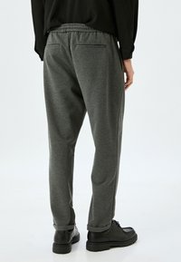 Grå joggingbukser lavet af blødt materiale. Elastisk talje, to baglommer og tapered ben. Parret med sorte sko.