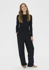 Crna majica dugih rukava i široke hlače, s ležernim krojem i elastičnim pojasom, upotpunjene svijetlim, uzorkovanim balerinkama.