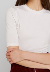 Bílý, přiléhavý tričko s krátkým rukávem a kulatým výstřihem. Měkká, hladká tkanina s mírným leskem, doplněná kordovou sukní.