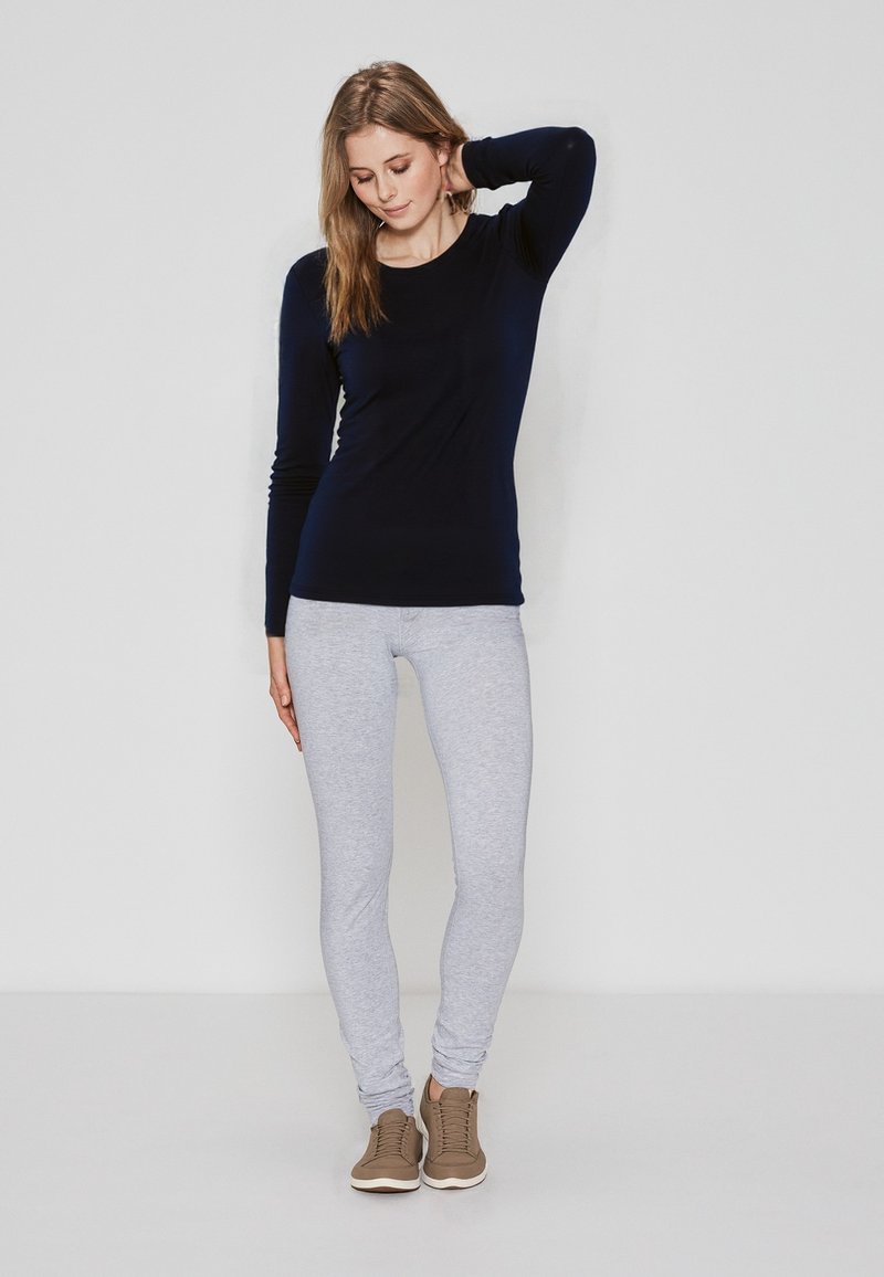 Marineblå langærmet top parret med lysegrå leggings og brune sneakers. Toppen er tætsiddende, mens leggingsene er stramme med en glat tekstur.