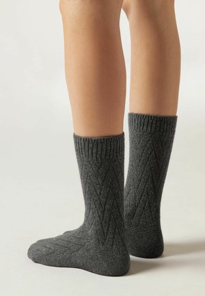 Calze grigie a maglia con polsini a coste e motivo a diamante diagonale. Il materiale appare texturizzato, coprendo le gambe inferiori fino alla caviglia.