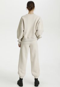 Felpa beige e joggers realizzati in tessuto morbido. Vestibilità ampia con polsini e vita a coste. Stivali neri completano il look.